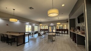 A spacious indoor area with multiple tables and chairs, ceiling lights, and a large screen on the right wall. - La Quinta Inn & Suites by Wyndham Albuquerque Midtown (Albuquerque)