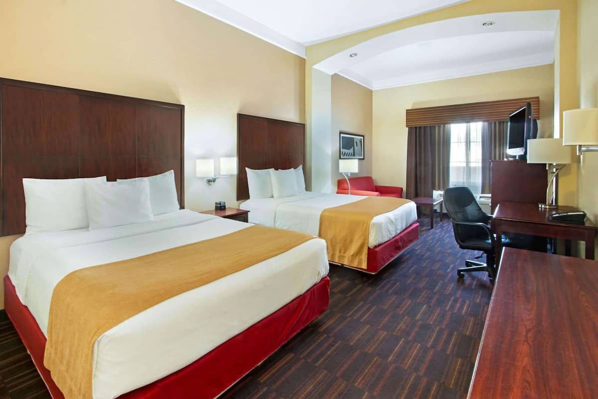 A hotel room with two beds, a desk, a chair, a TV, and a window with curtains.