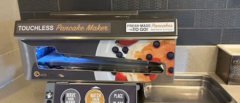 A touchless pancake maker with a digital display and a stainless steel plate underneath.