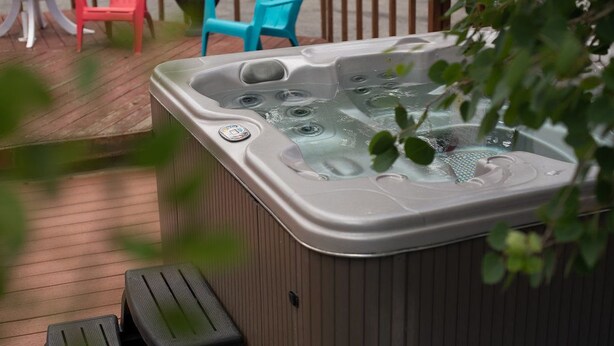 Un jacuzzi en una terraza de madera, con dos sillas reclinables negras y una silla roja y una azul al fondo.