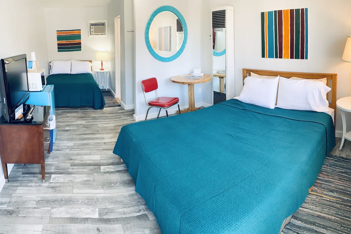 A hotel room with two beds, a desk, a chair, and a small table.