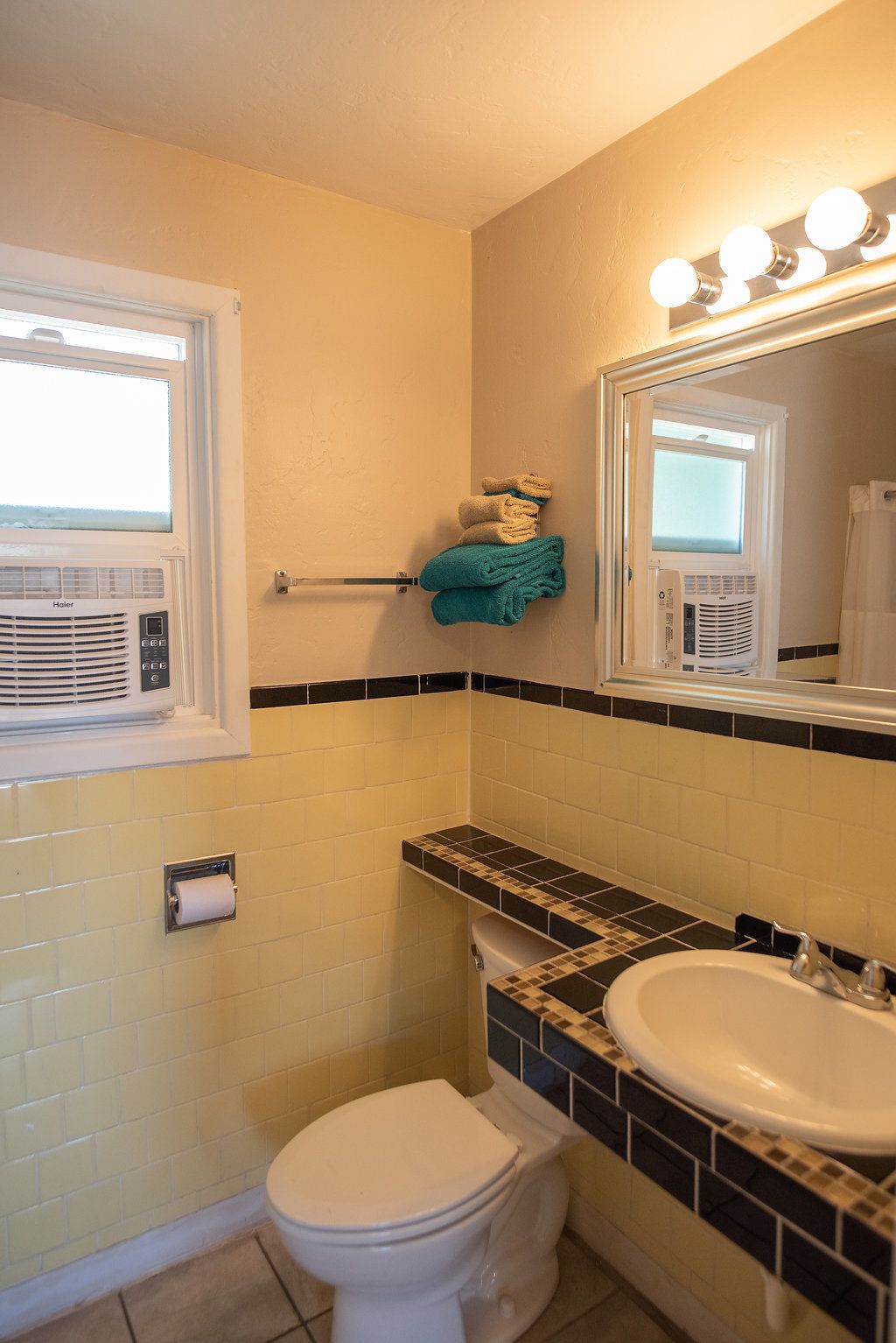 A bathroom with a toilet, sink, towel rack, and a window with a heater.