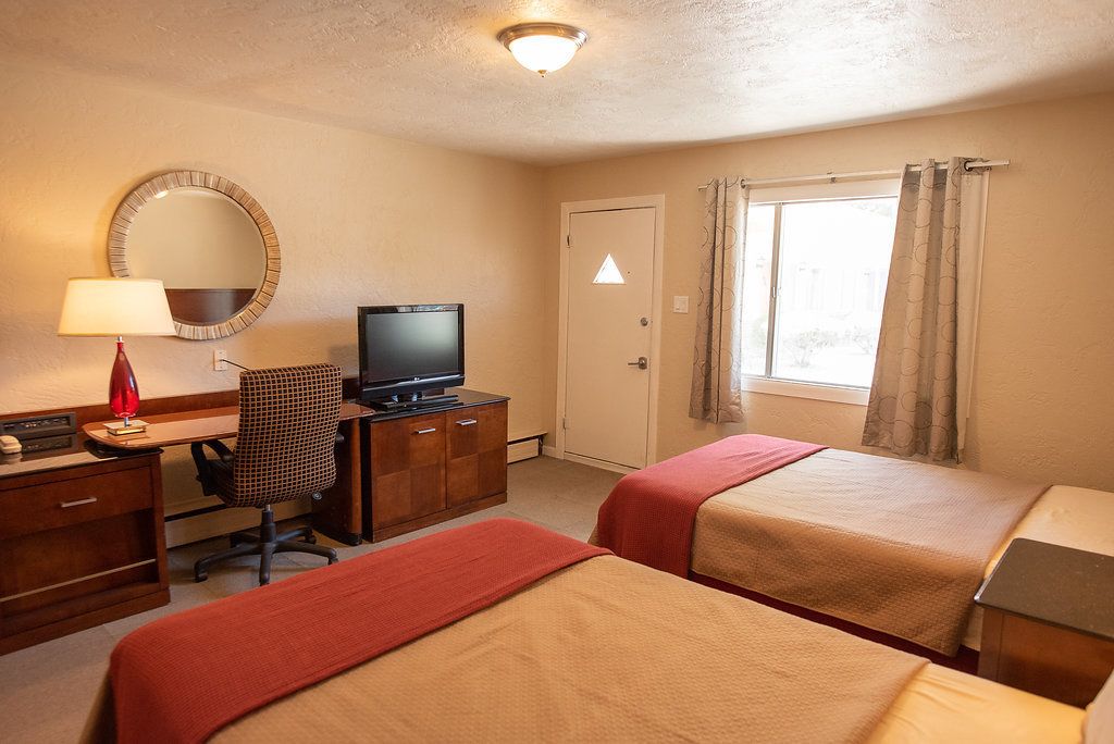 A hotel room with two beds, a desk with a television, a chair, and a lamp.