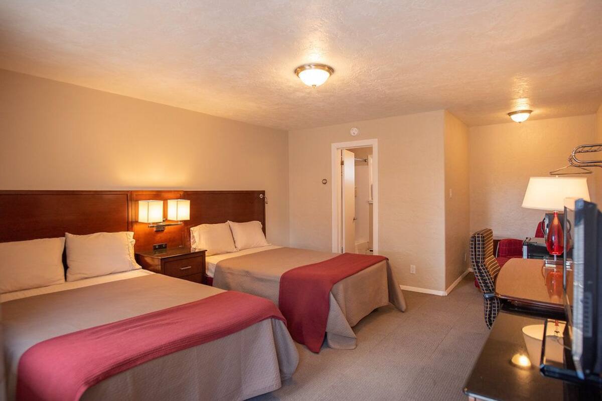 A hotel room with two beds, a desk with a chair, and a TV.