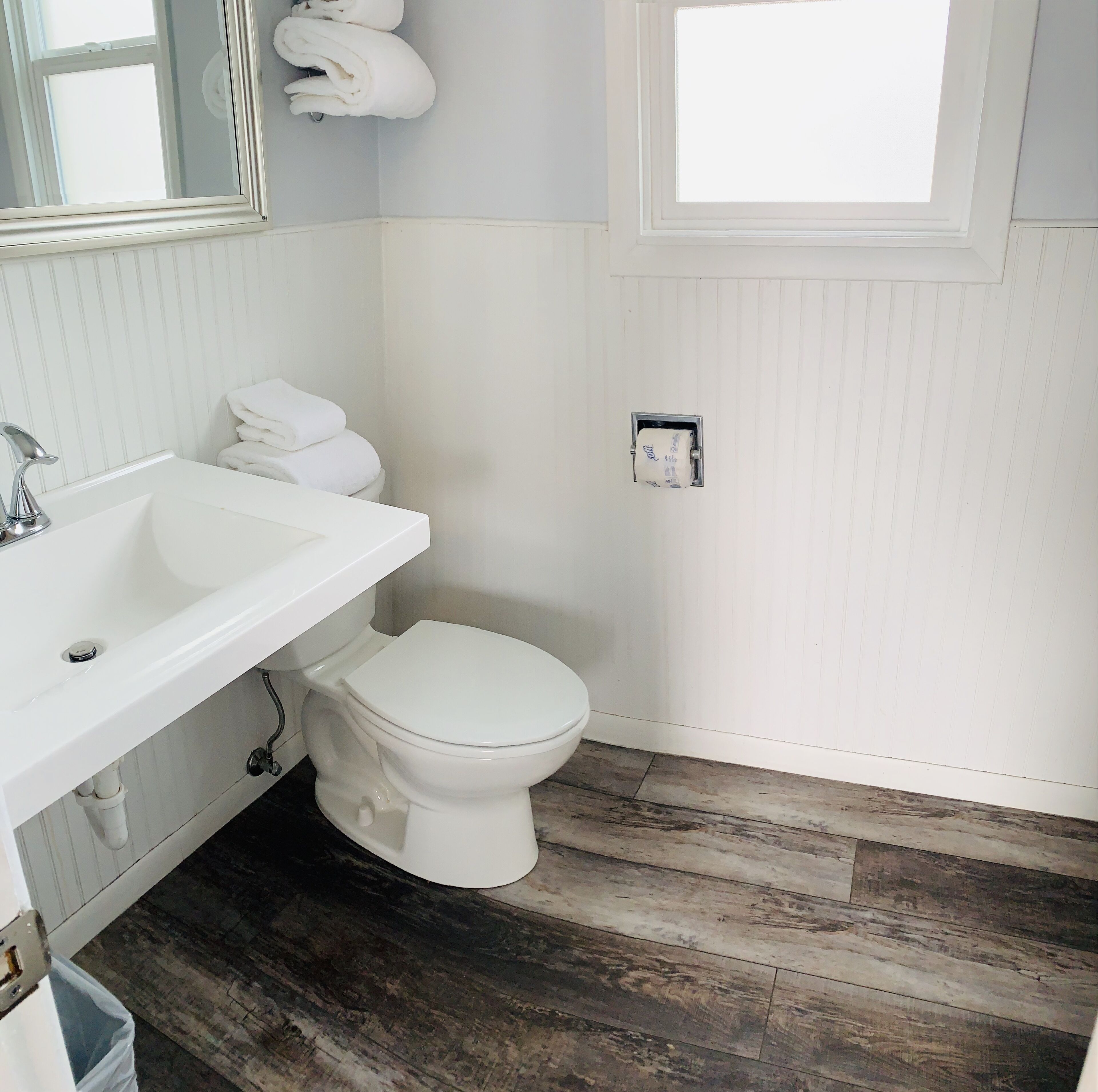 Un baño con lavamanos blanco, inodoro y suelo de madera.