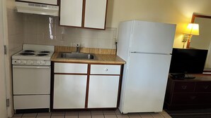 A compact kitchen with a stove, sink, and refrigerator, featuring wooden cabinets and a tiled backsplash. - Gulf Way Inn (Clearwater)