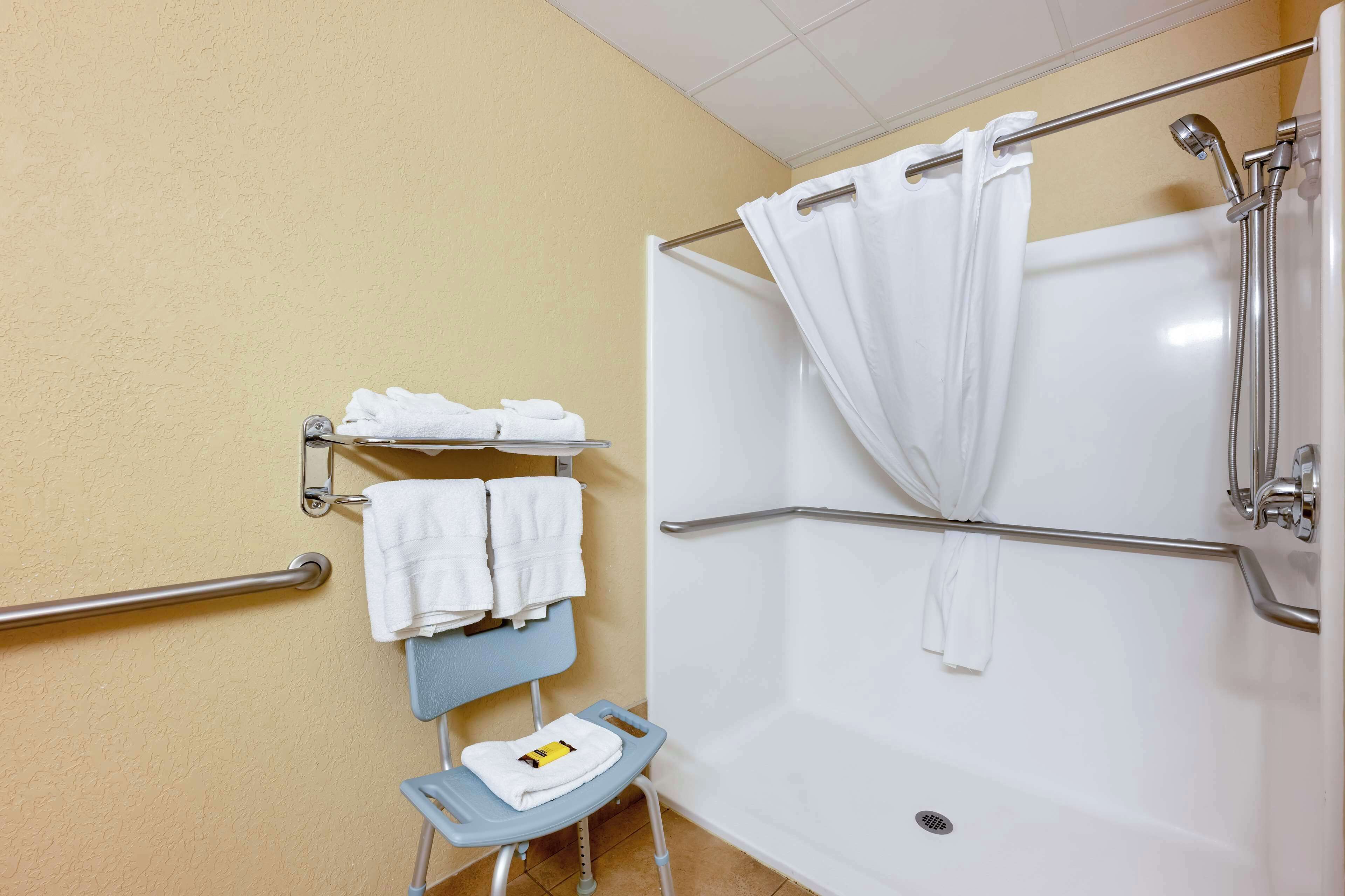 A bathroom with a white bathtub, a shower, a grab bar, a towel rack, and a wheelchair-accessible bench.
