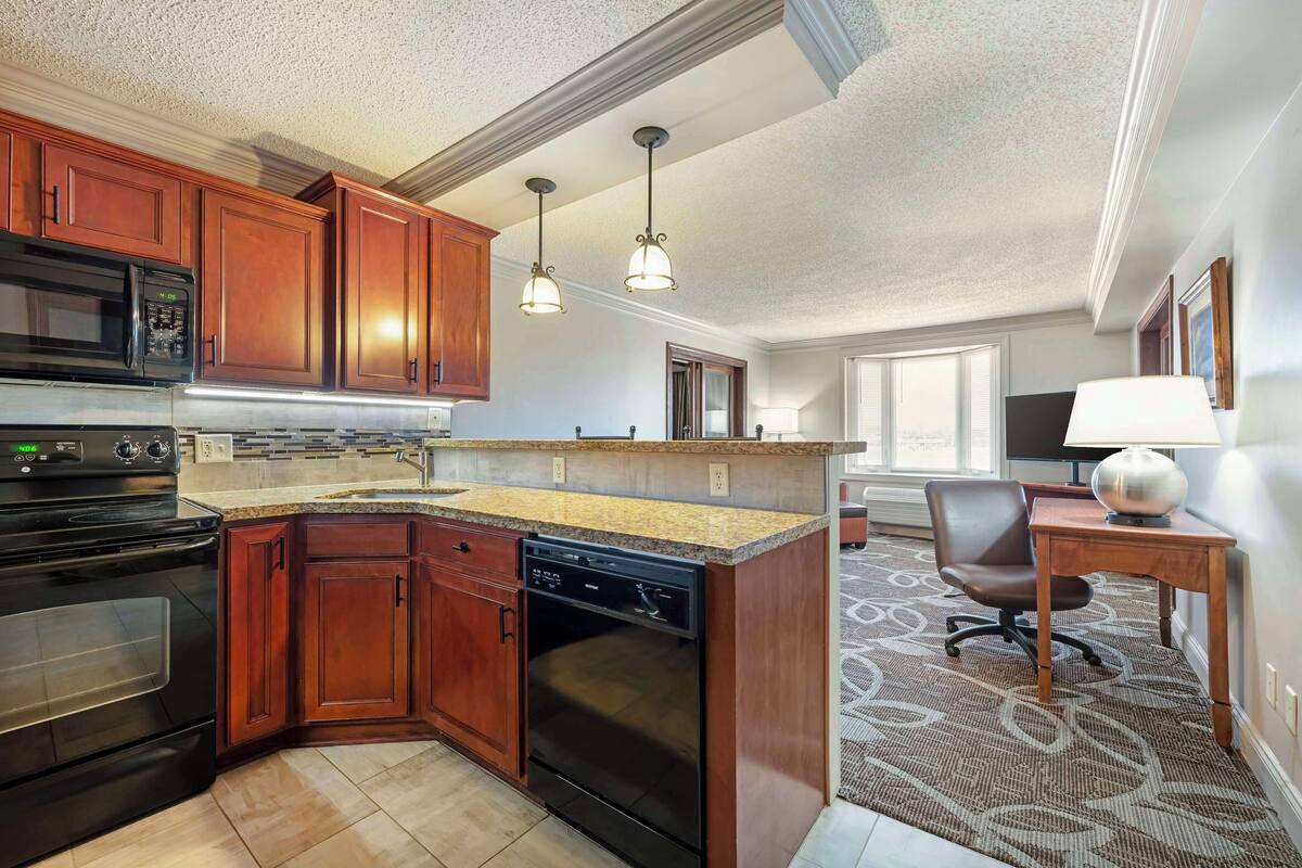 A kitchen with wooden cabinets, a microwave, an oven, and a dishwasher. There is a dining area with a table and chairs.