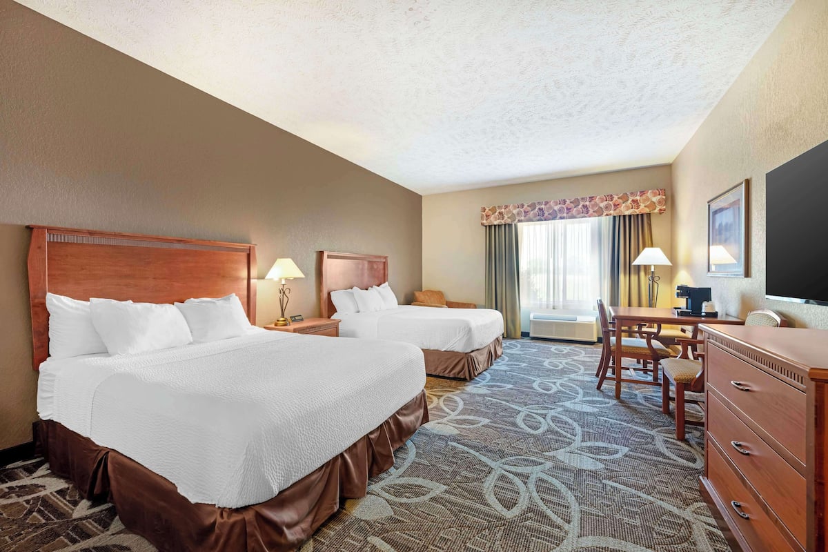 A hotel room with two beds, a desk, a chair, a dresser, and a television.