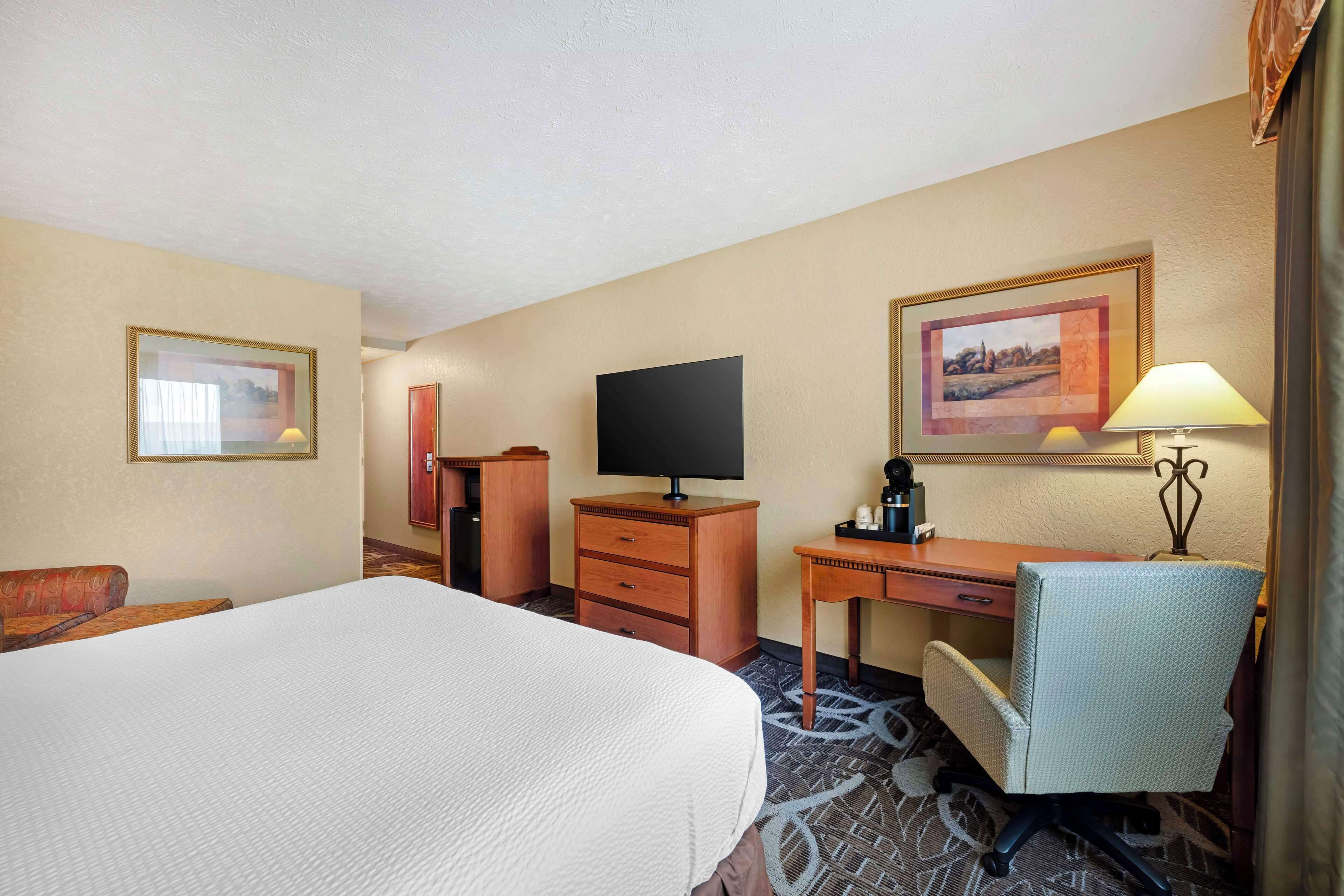Una habitación de hotel con una cama grande, un escritorio, una silla, un televisor y una lámpara.
