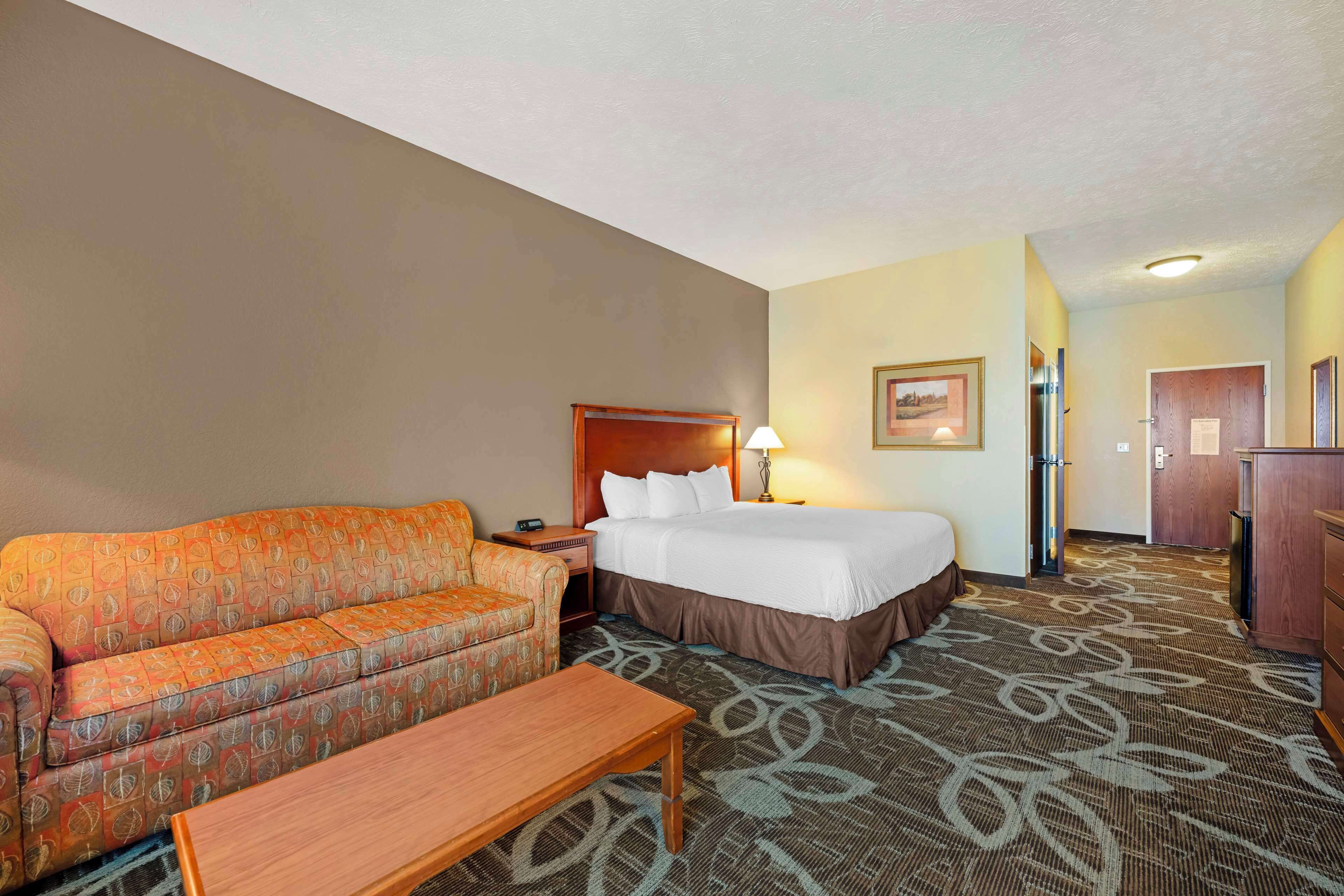 A hotel room with a bed, a sofa, a desk, and a carpeted floor.