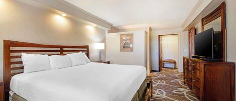 Une chambre d’hôtel avec un grand lit, une commode en bois, une télévision et une moquette à motifs.