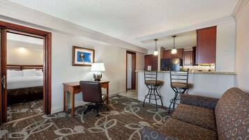 A hotel room with a bed, a desk, a chair, a sofa, and a kitchenette.