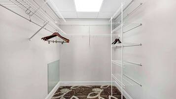 Un dressing ouvert avec de nombreuses étagères métalliques blanches et un tapis à motifs sur le sol.