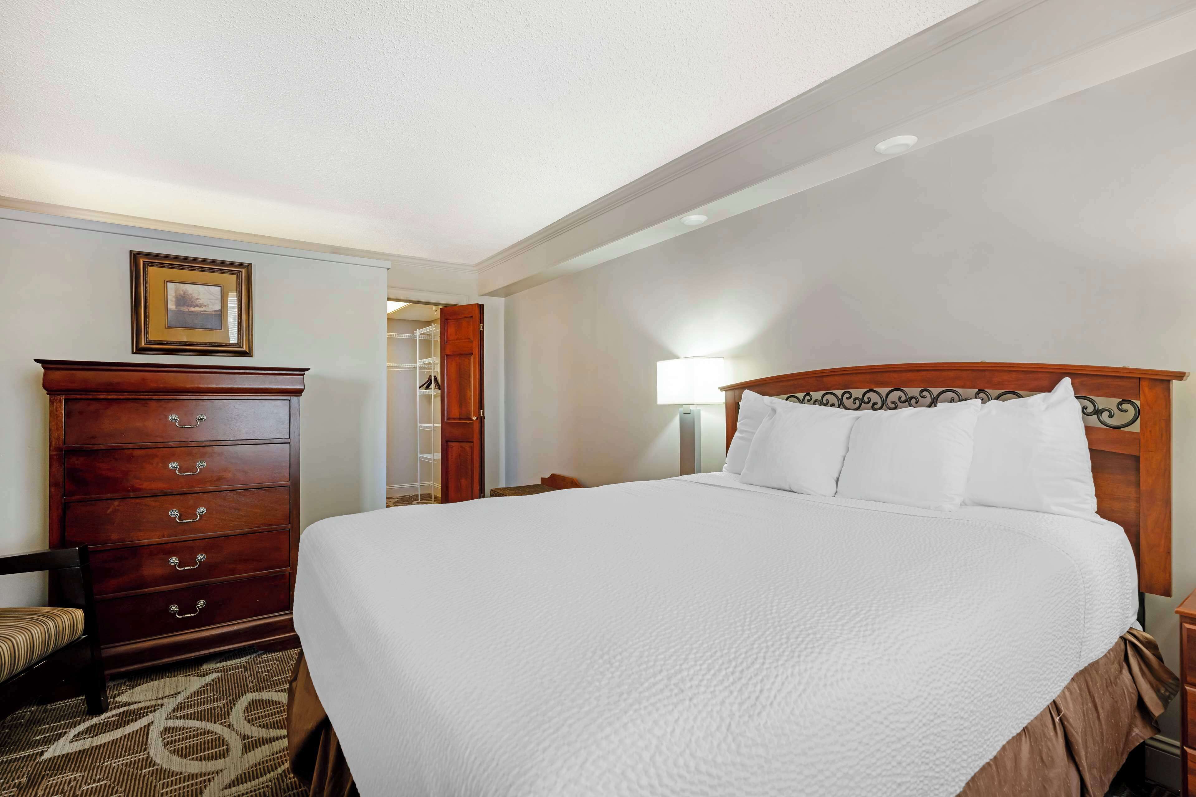 Une chambre d’hôtel avec un grand lit, une commode en bois, une chaise et une table de chevet avec une lampe.