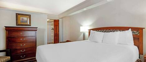 A hotel room with a large bed, a wooden dresser, a chair, and a nightstand with a lamp.