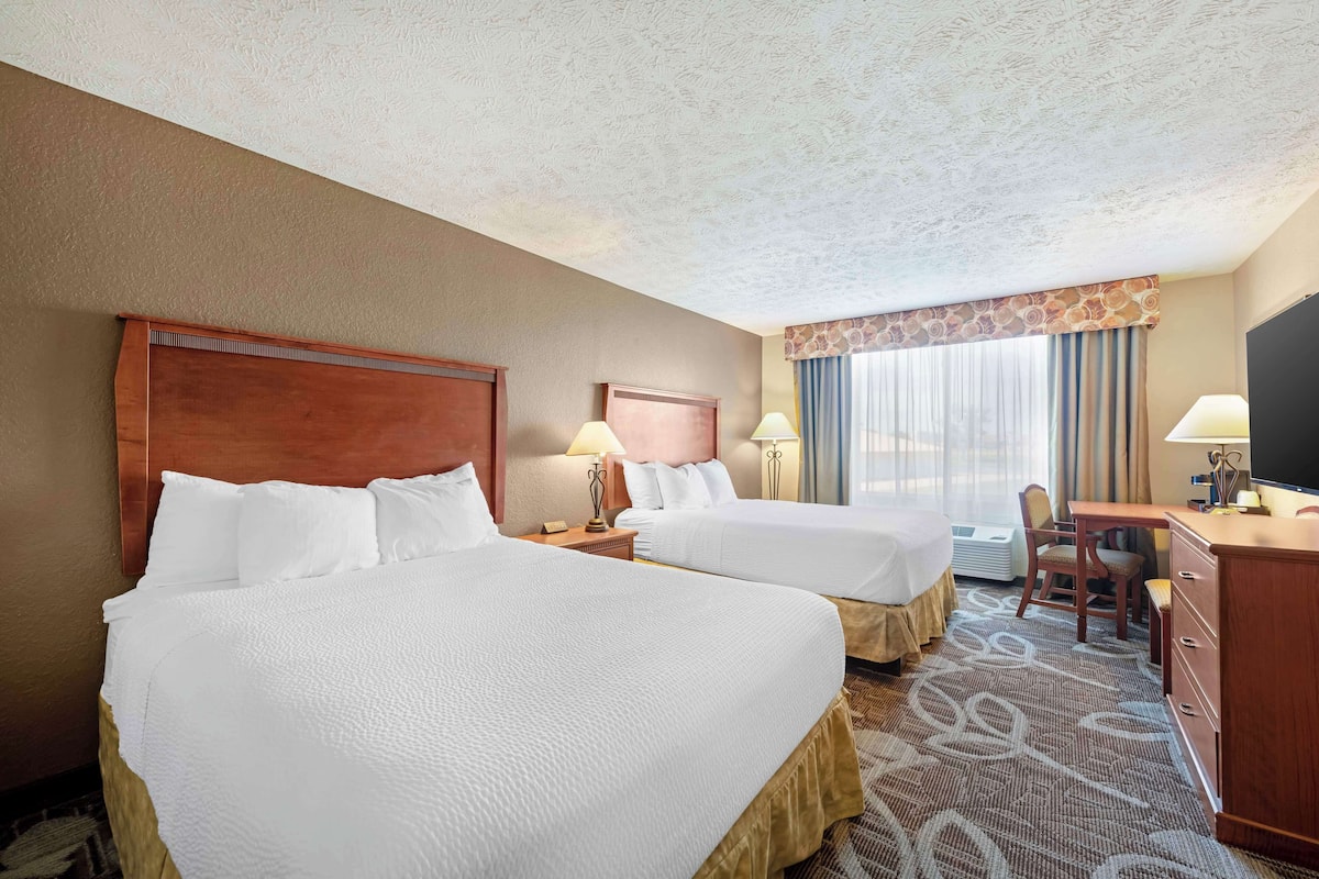 A hotel room with two beds, a desk, a chair, a television, and a window with curtains.