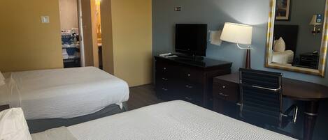 A hotel room with two beds, a desk, a television, a mirror, and a bathroom visible through an open door.