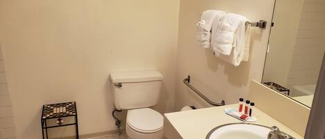A small bathroom with a toilet, a sink, and a mirror. There is a small table with a chessboard and a towel rack with towels.