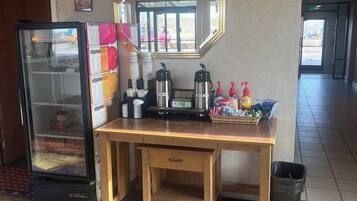 A hotel room with a wooden desk, a refrigerator, a coffee station, and a patterned rug.