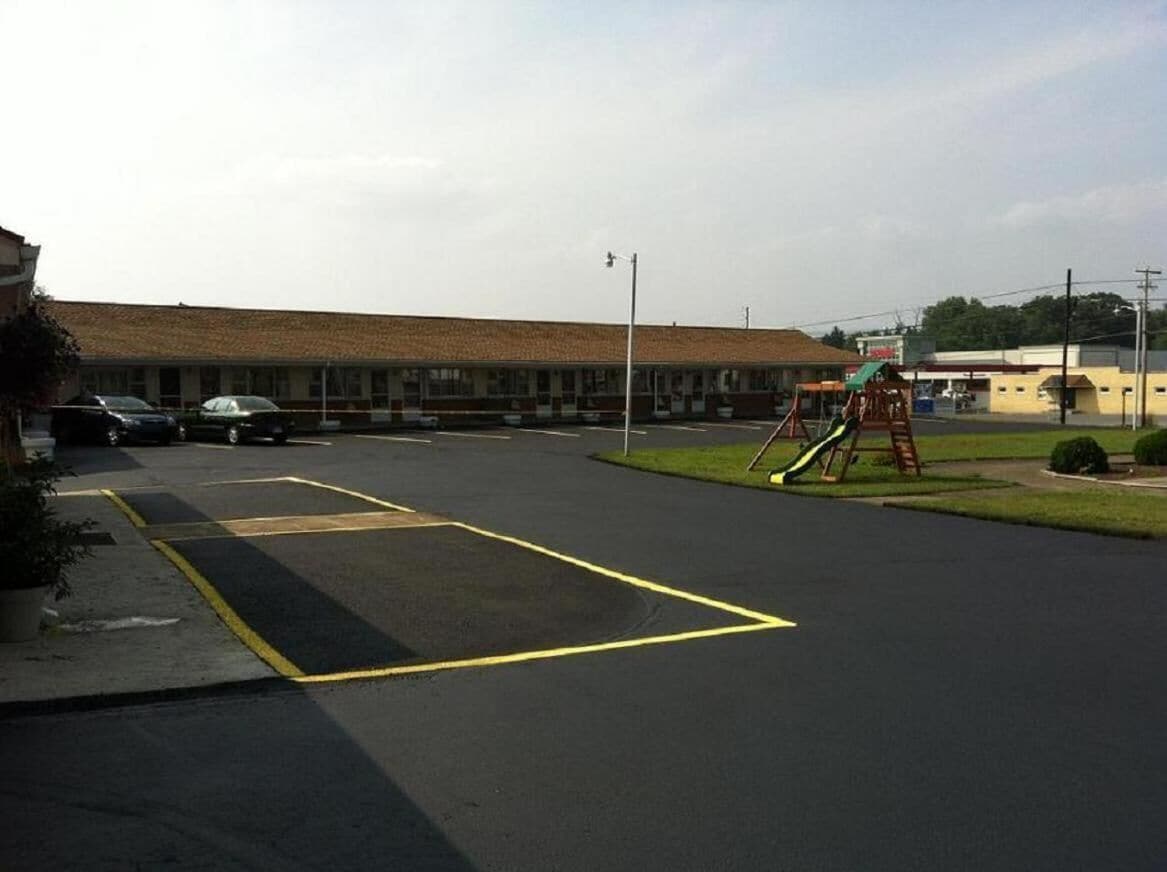 A parking lot with marked spaces, a playground with a slide, and a building with a tiled roof in the background.