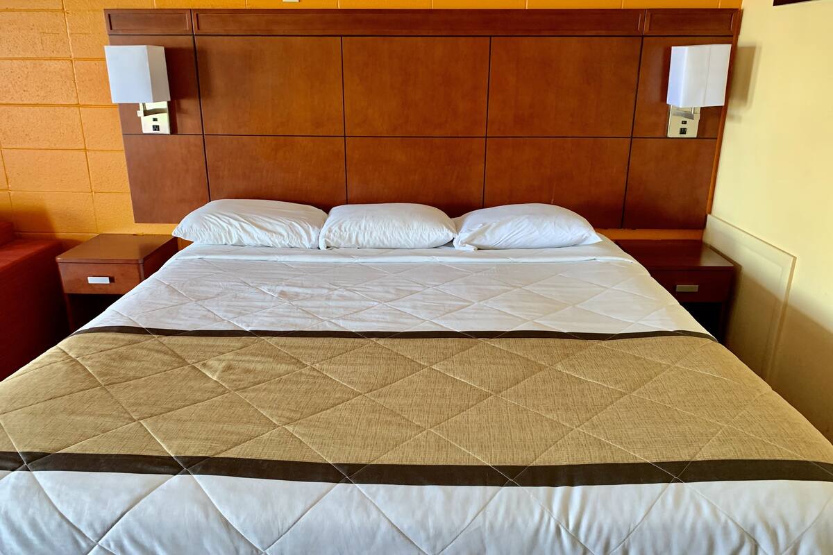 A hotel room with a large bed, wooden headboard, two bedside tables, and a red chair.