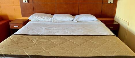A hotel room with a large bed, wooden headboard, two bedside tables, and a red chair.