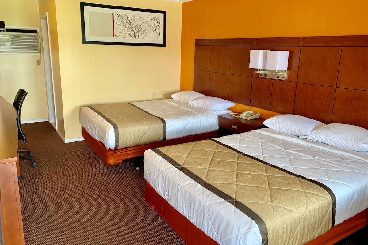 A hotel room with two beds, a desk, a chair, a telephone, and a wall-mounted light fixture.