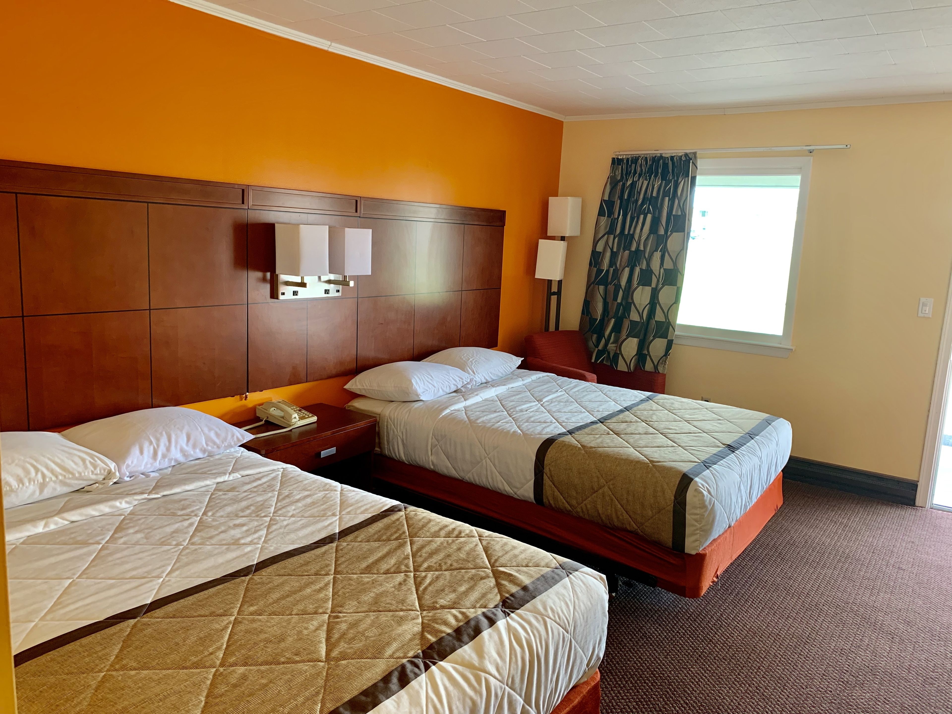 A hotel room with two beds, a wooden headboard, a nightstand with a phone, and a window with curtains.