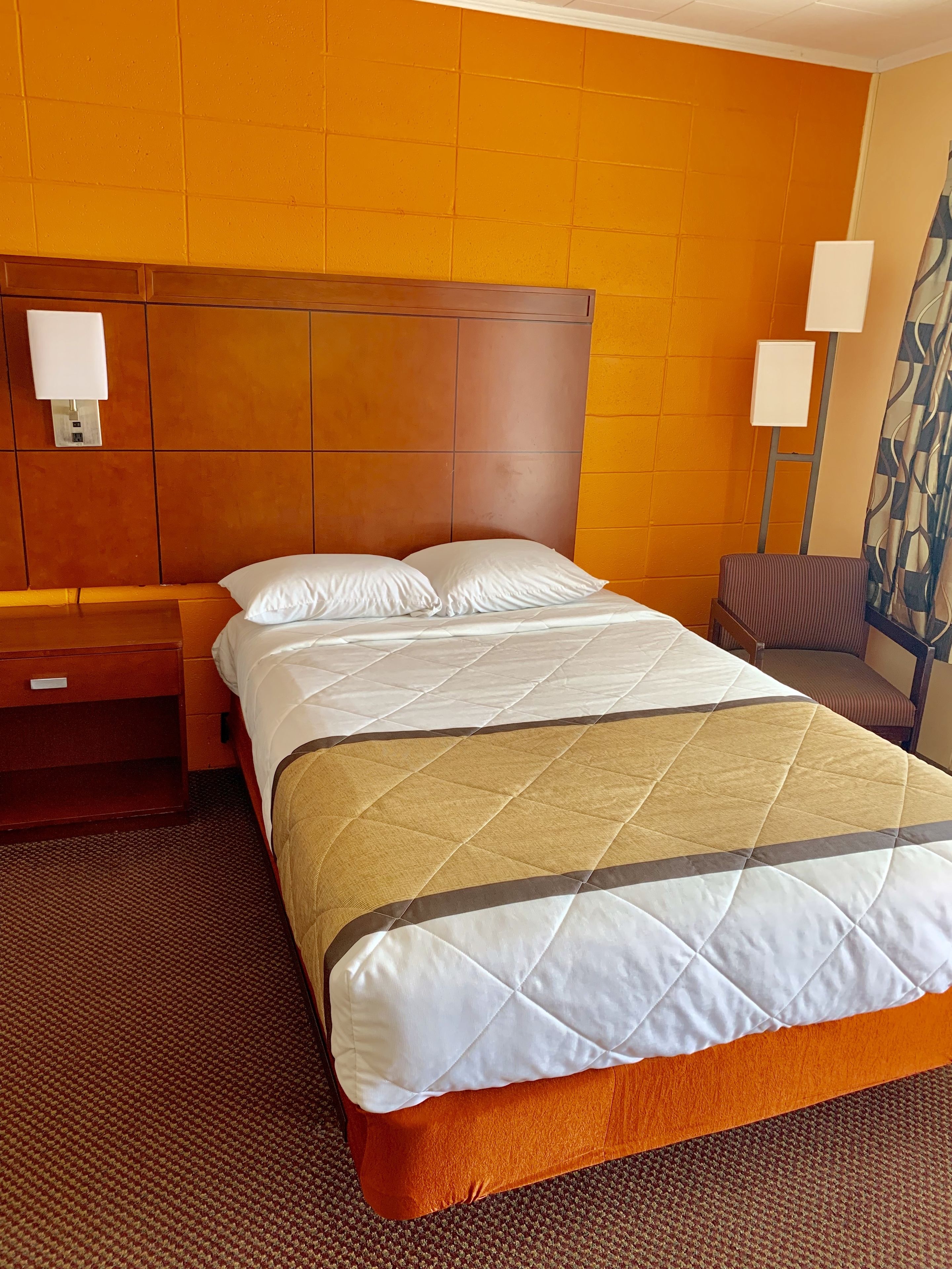 A hotel room with a large bed, wooden headboard, two bedside tables, and a patterned wall.