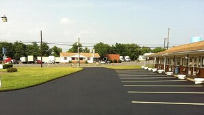 A motel with a parking lot, a row of rooms, and a small building in the background. - Budget Inn (Mifflintown)