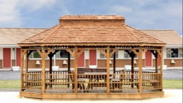 A wooden gazebo with a tiled roof, surrounded by a building with red and white walls. - Budget Inn (Mifflintown)