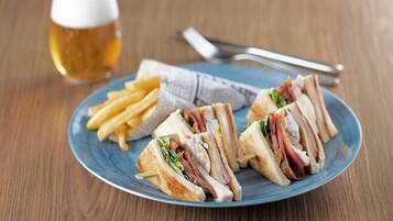 Un plato con un sándwich y papas fritas, una jarra de cerveza y cubiertos sobre una mesa de madera.