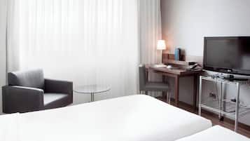 A hotel room with a bed, a desk with a computer, a chair, a TV, and a small table.