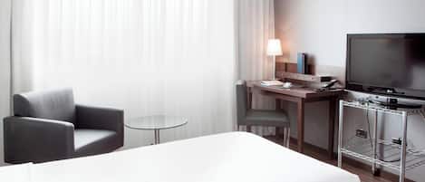 Habitación de hotel con cama, escritorio, computadora, silla, televisor y una mesita.