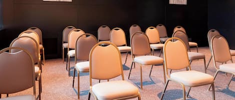Un salón de conferencias con hileras de sillas color beige y piso alfombrado.