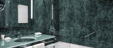 Un baño moderno con ducha envuelta en vidrio, una bañera blanca y pared con azulejos de mármol.