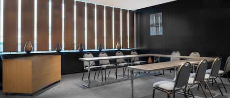 Un salón de conferencias con una larga mesa, sillas, un mostrador de recepción de madera y persianas verticales.