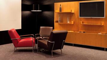 Un salón de conferencias con tres sillas, un televisor de pantalla plana grande y un mueble de madera con estantes.