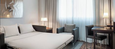 Una habitación de hotel con una cama, un escritorio, una silla y una lámpara.