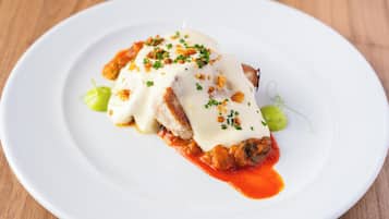 Un plato blanco con un alimento cubierto de salsa y decorado con hierbas verdes.