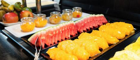 Un bufé con sandía en rodajas, naranjas y pequeños frascos de conservas de frutas.
