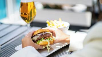 A person holding a burger and fries with a glass of beer on a table.