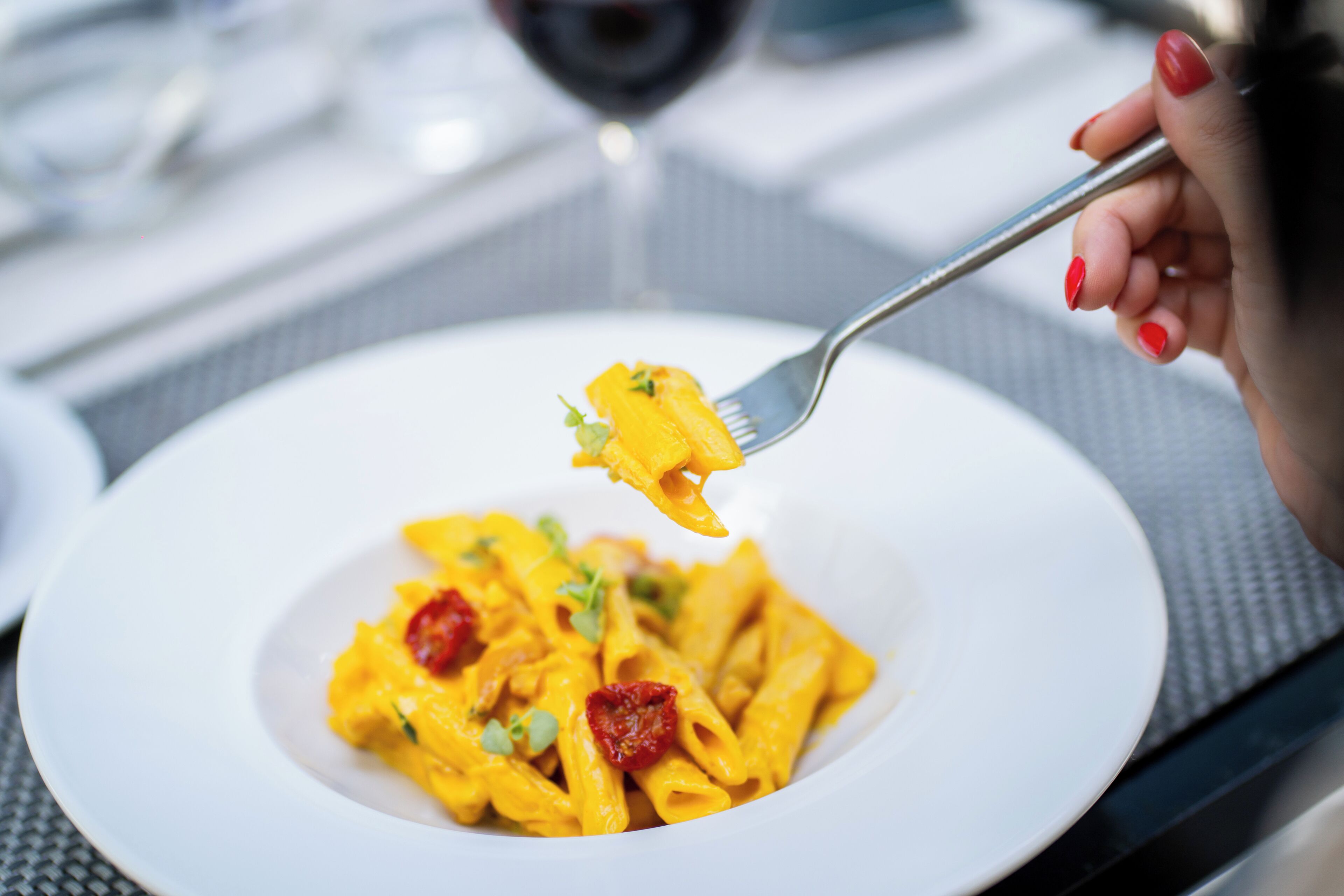 A white plate with pasta and a fork lifting a piece of pasta.