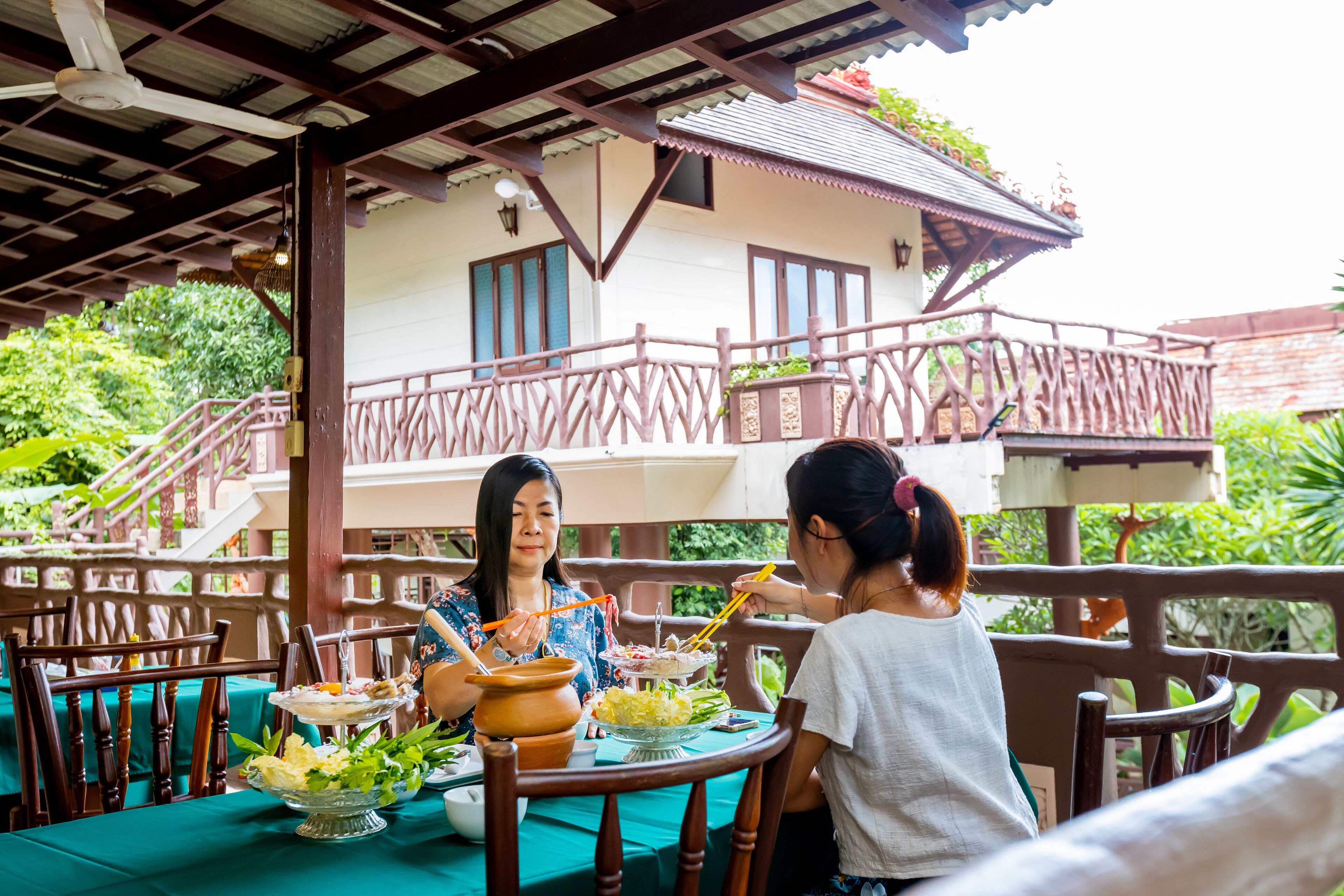 Un espacio de comedor al aire libre con muebles de madera y una mesa dispuesta con vajilla y una olla.