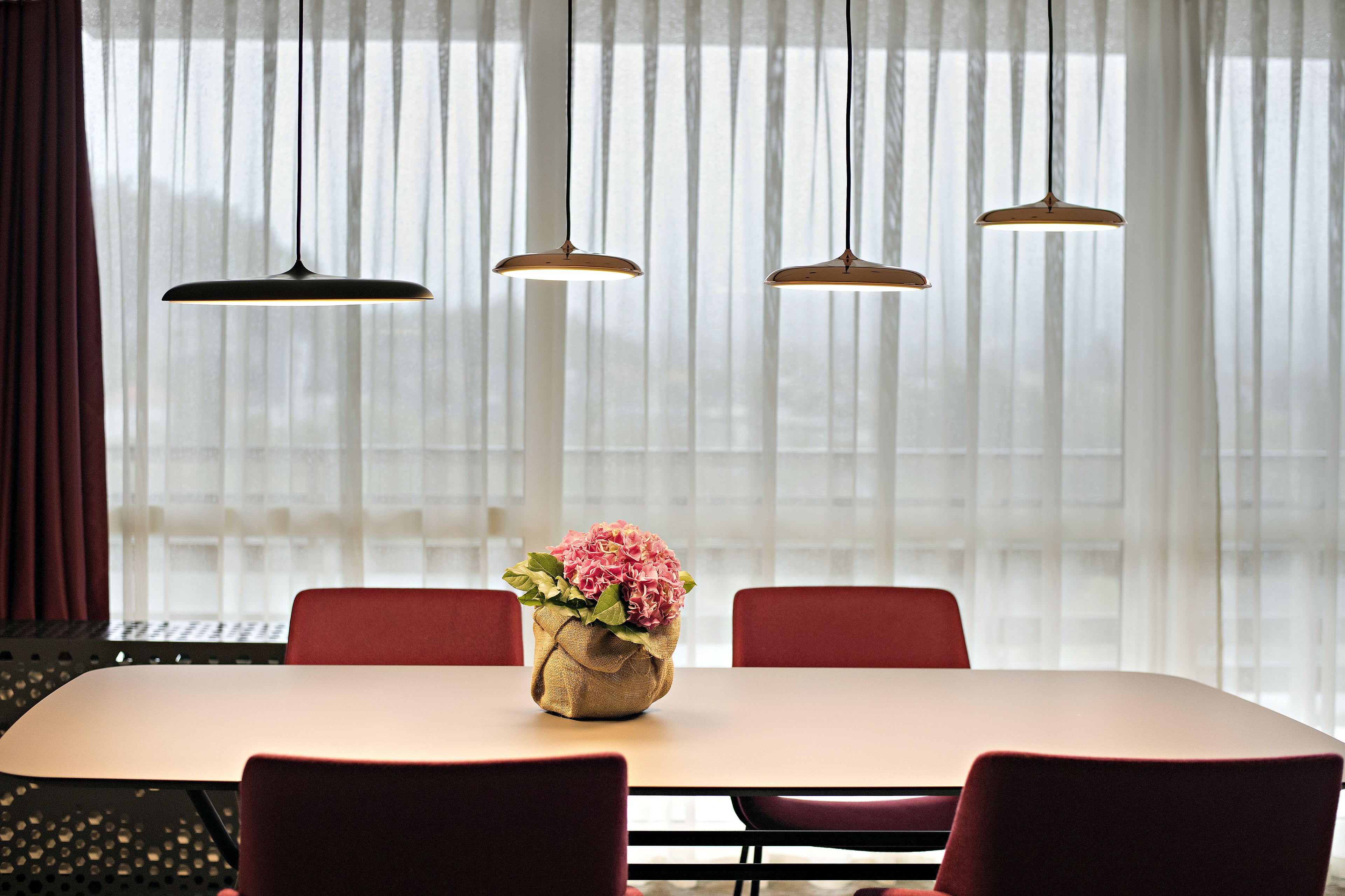 A dining area with a table, chairs, hanging pendant lights, and a vase with flowers.