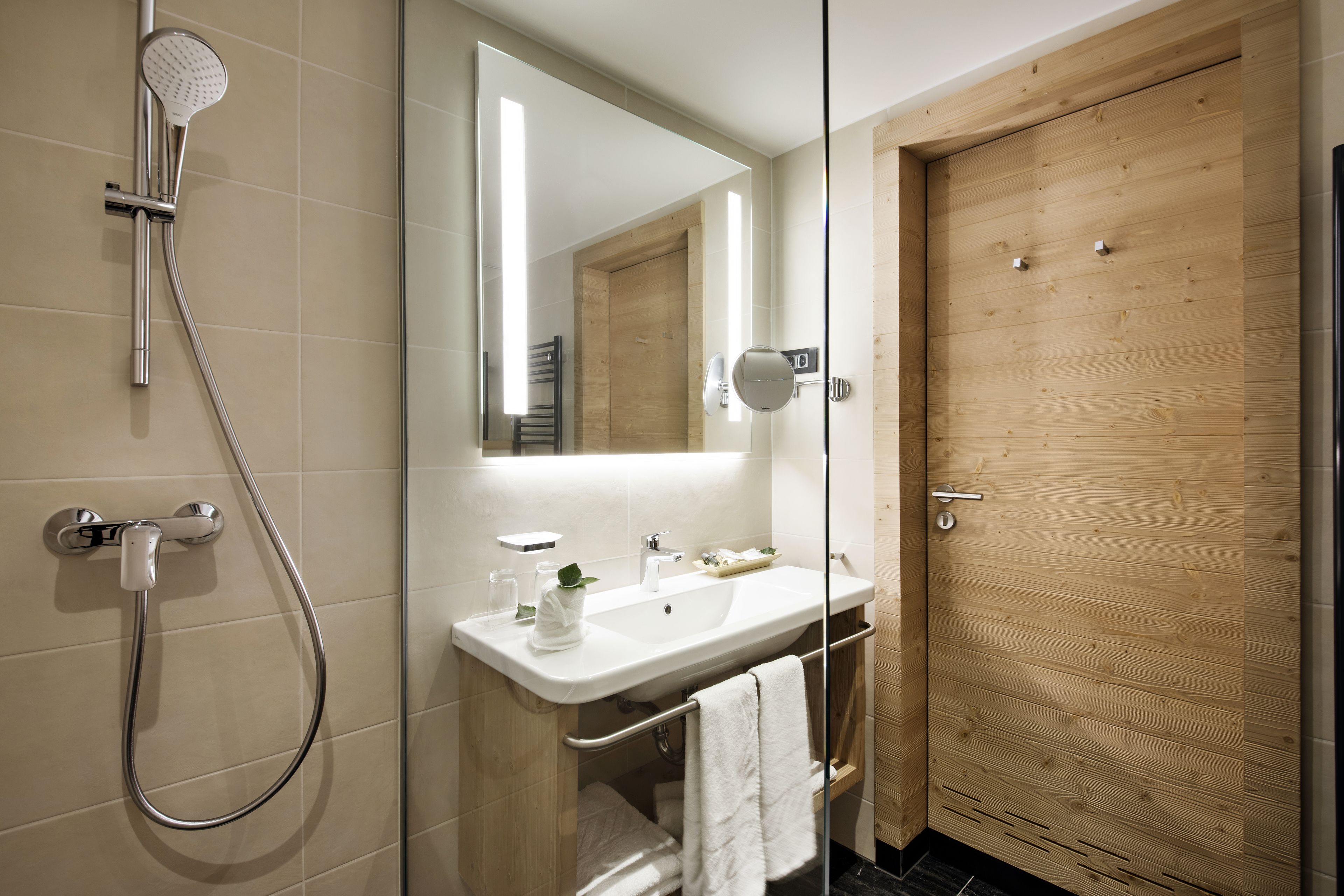 A modern bathroom with a glass-enclosed shower, a wooden door, and a white sink with a towel rack.