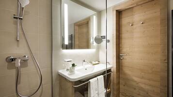 Un baño moderno con cabina de ducha de vidrio, puerta de madera y lavamanos blanco con toallero.