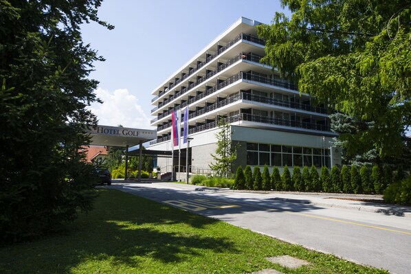 A multi-story hotel with balconies, a covered entrance, and a well-maintained lawn.