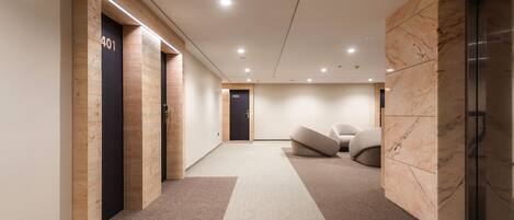 A modern hallway with wooden and marble walls, numbered doors, and a central seating area.